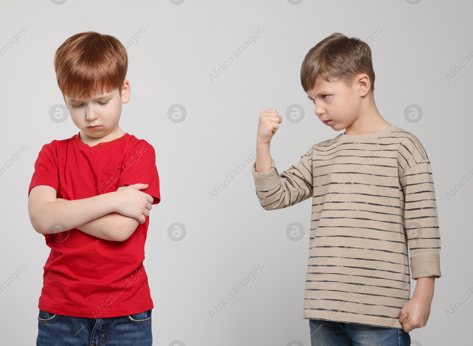 Photo of Boy with clenched fist looking at scared kid on light grey background. Children's bullying
