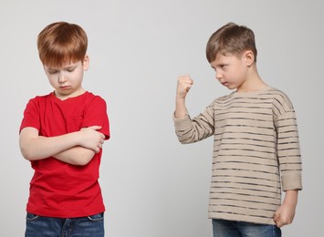 Boy with clenched fist looking at scared kid on light grey background. Children's bullying