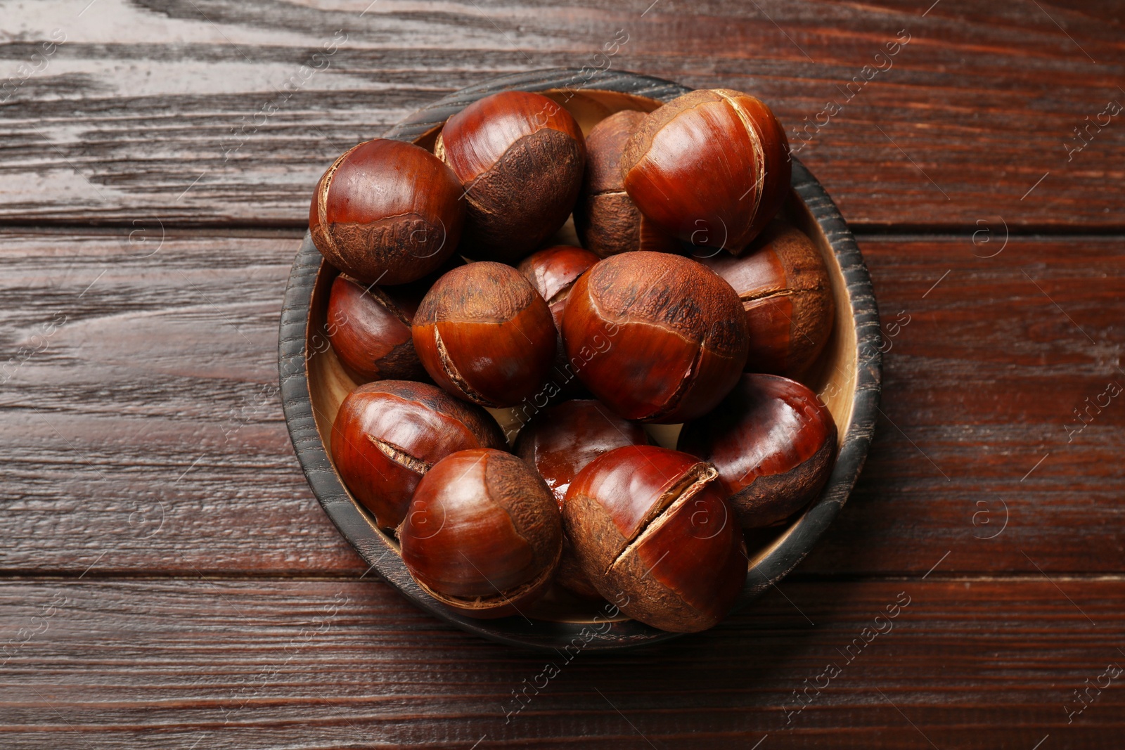 Photo of Roasted edible sweet chestnuts on wooden table, top view