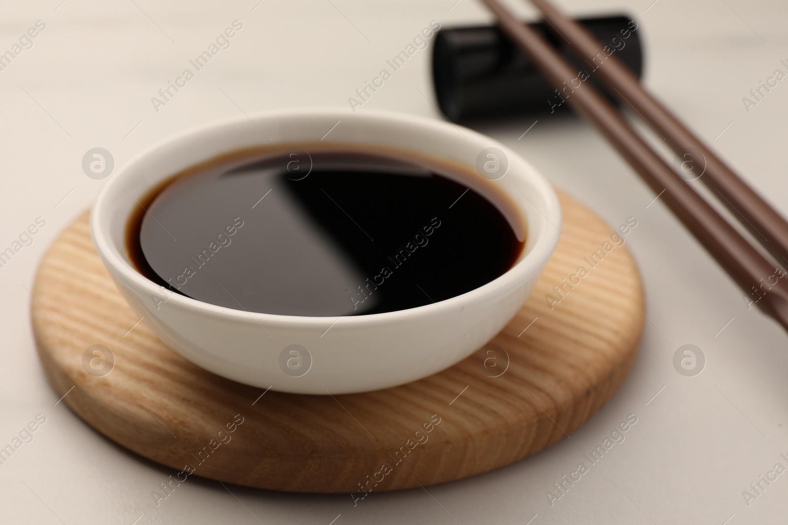 Photo of Bowl with soy sauce and chopsticks on white table, closeup