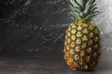 Whole ripe pineapple on grey table near black wall. Space for text