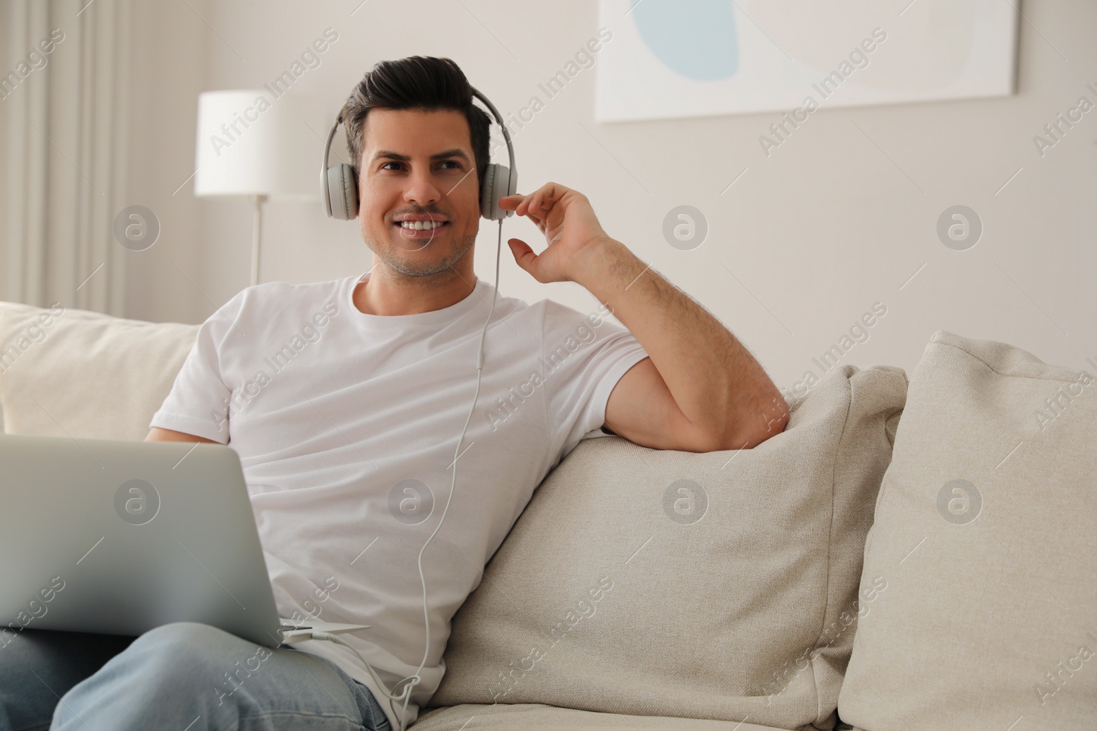 Photo of Man with laptop and headphones sitting on sofa at home