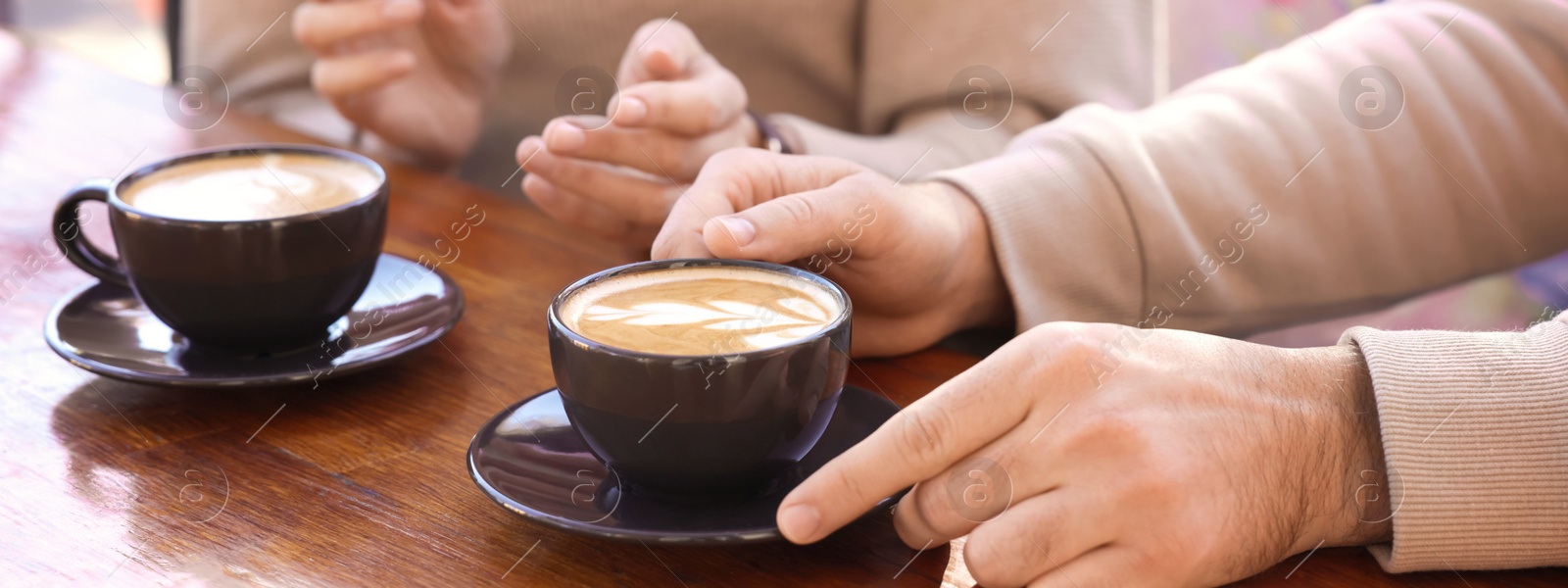 Image of People with cups of aromatic coffee at wooden table, closeup. Banner design