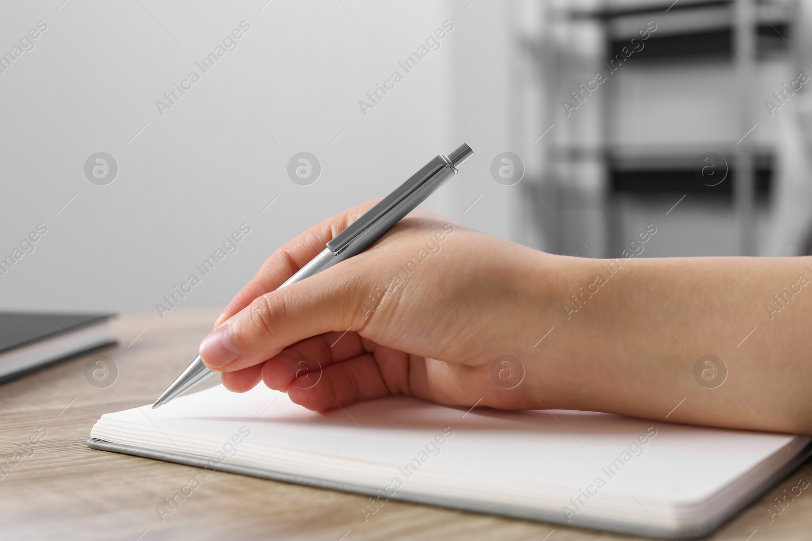 Photo of Woman writing in notebook at wooden table indoors, closeup