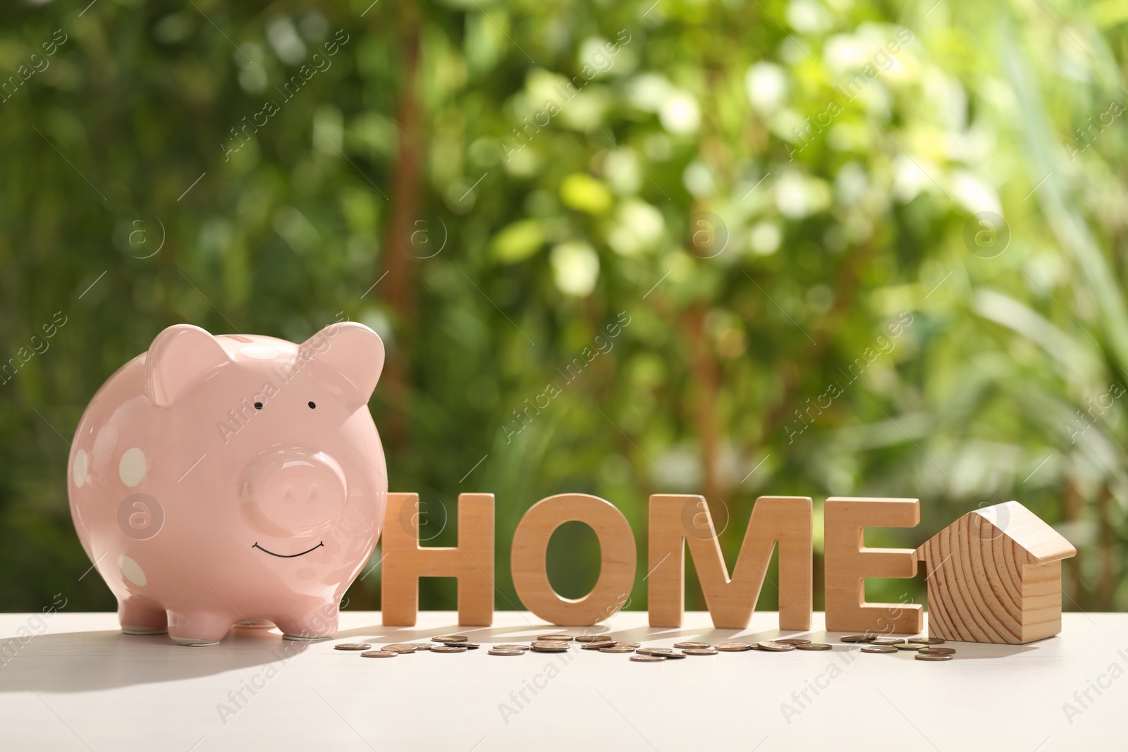 Photo of Piggy bank, word Home, house model and coins on table outdoors. Saving money concept