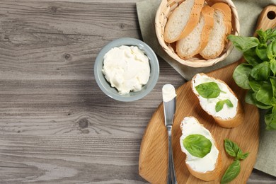 Photo of Delicious sandwiches with cream cheese and basil leaves on wooden table, flat lay. Space for text