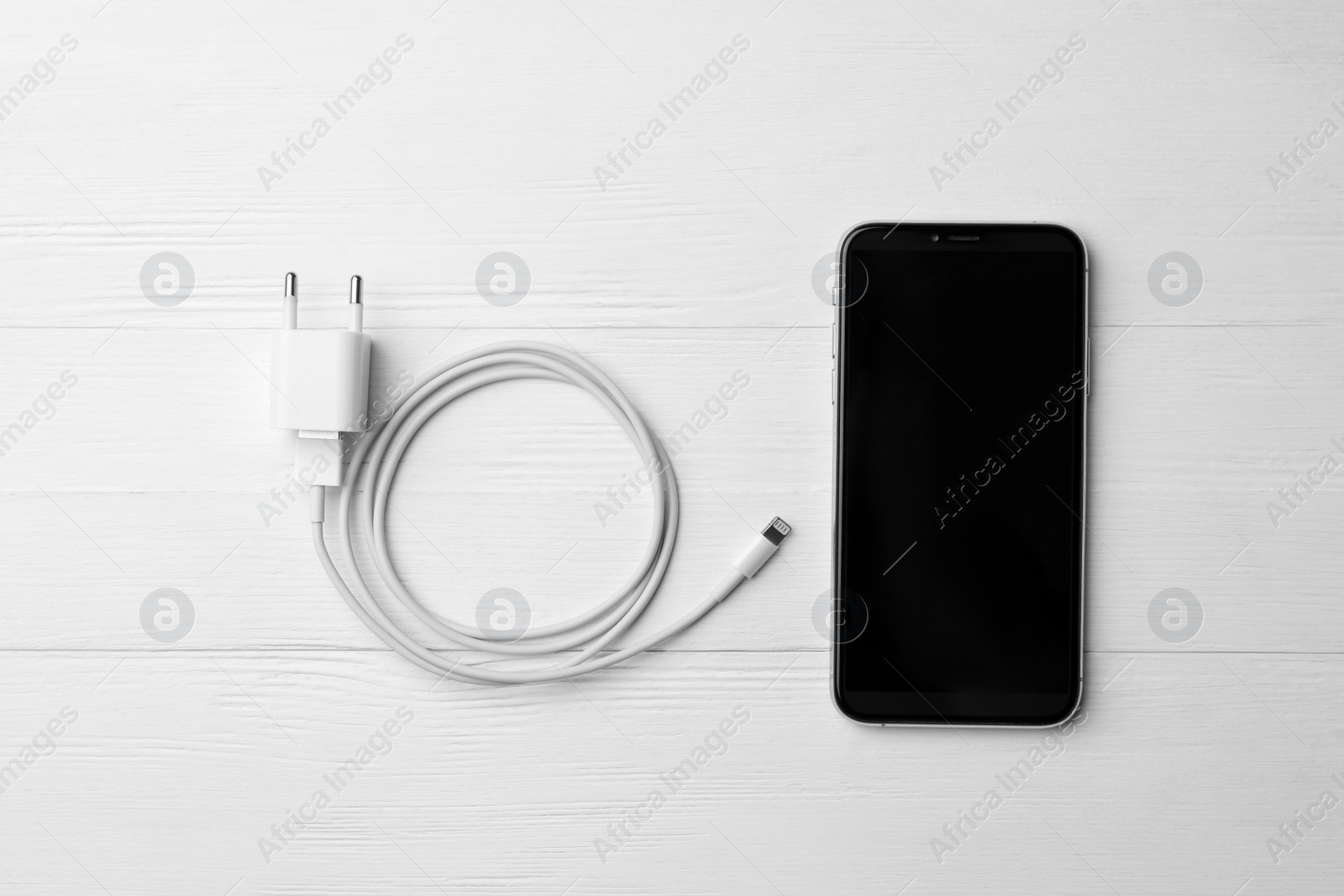 Photo of Smartphone and USB charger on white wooden table, flat lay. Modern technology