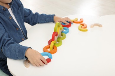 Photo of Motor skills development. Boy playing with colorful wooden arcs at white table, closeup. Space for text