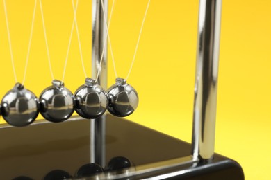 Photo of Newton's cradle on yellow background, closeup. Physics law of energy conservation