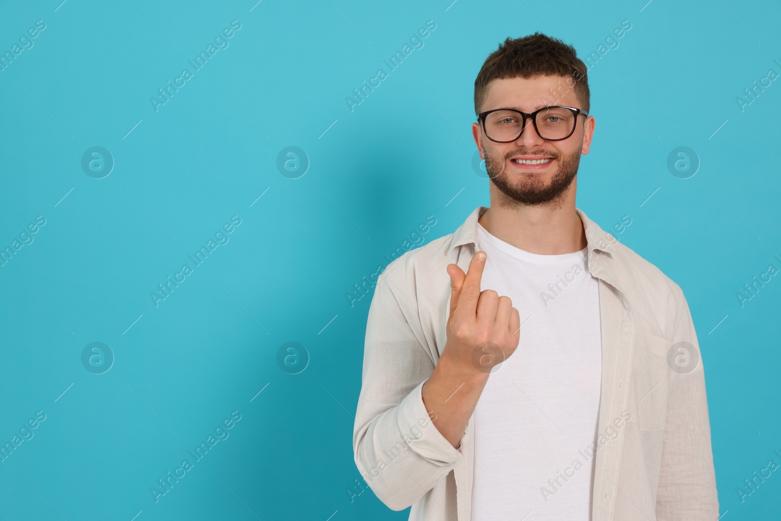 Photo of Young man showing heart gesture on light blue background, space for text