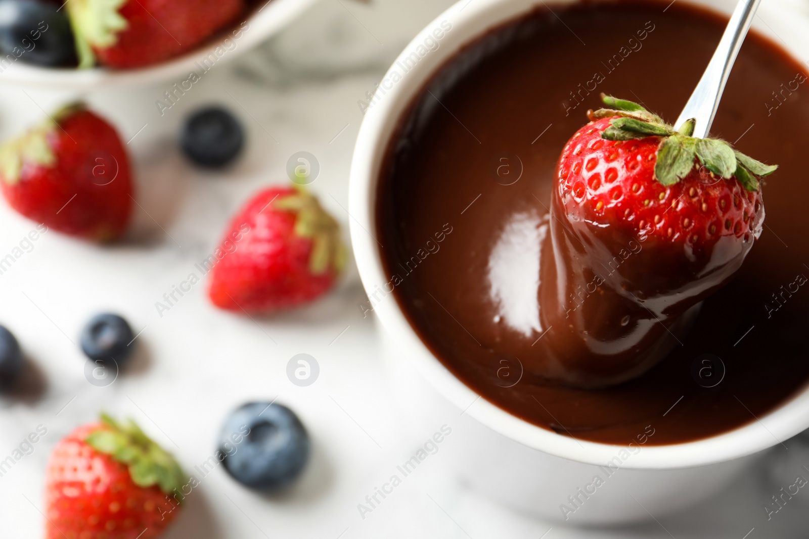 Photo of Dipping strawberry into fondue pot with chocolate on white table, top view