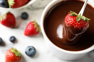 Dipping strawberry into fondue pot with chocolate on white table, top view