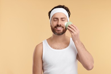 Photo of Man with headband washing his face using sponge on beige background