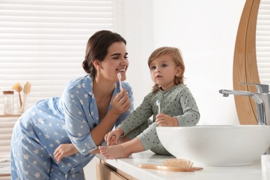 Photo of Mother and her daughter brushing teeth together in bathroom