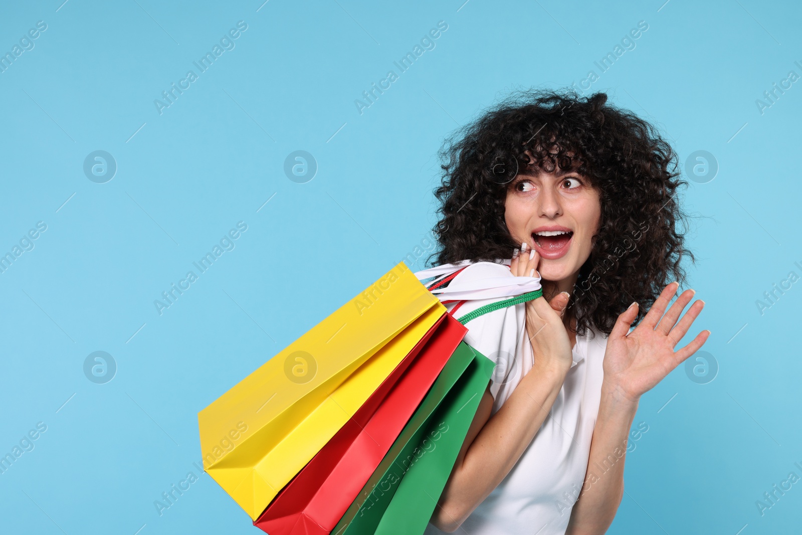 Photo of Happy young woman with shopping bags on light blue background. Space for text