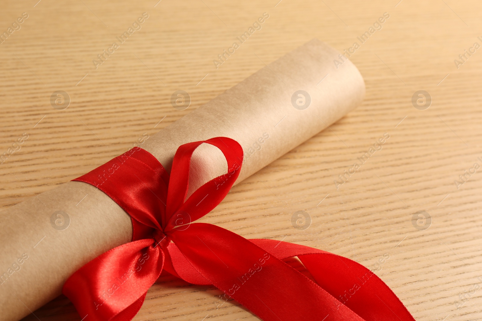 Photo of Graduation diploma tied with red ribbon on wooden table, closeup