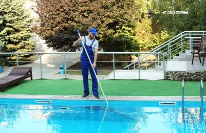 Male worker cleaning outdoor pool with scoop net