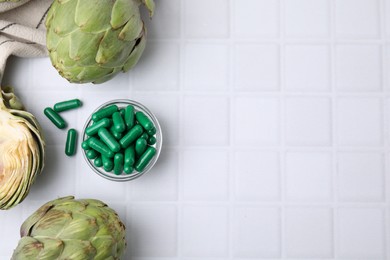 Photo of Bowl with pills and fresh artichokes on white tiled table, flat lay. Space for text