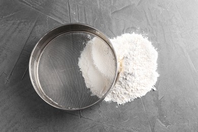 Photo of Metal sieve and flour on grey table, top view