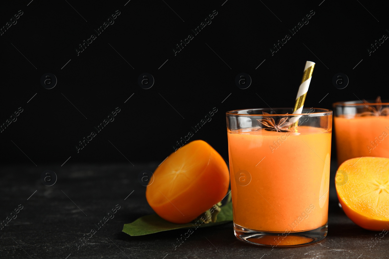 Photo of Tasty persimmon smoothie with anise and fresh fruits on black table. Space for text