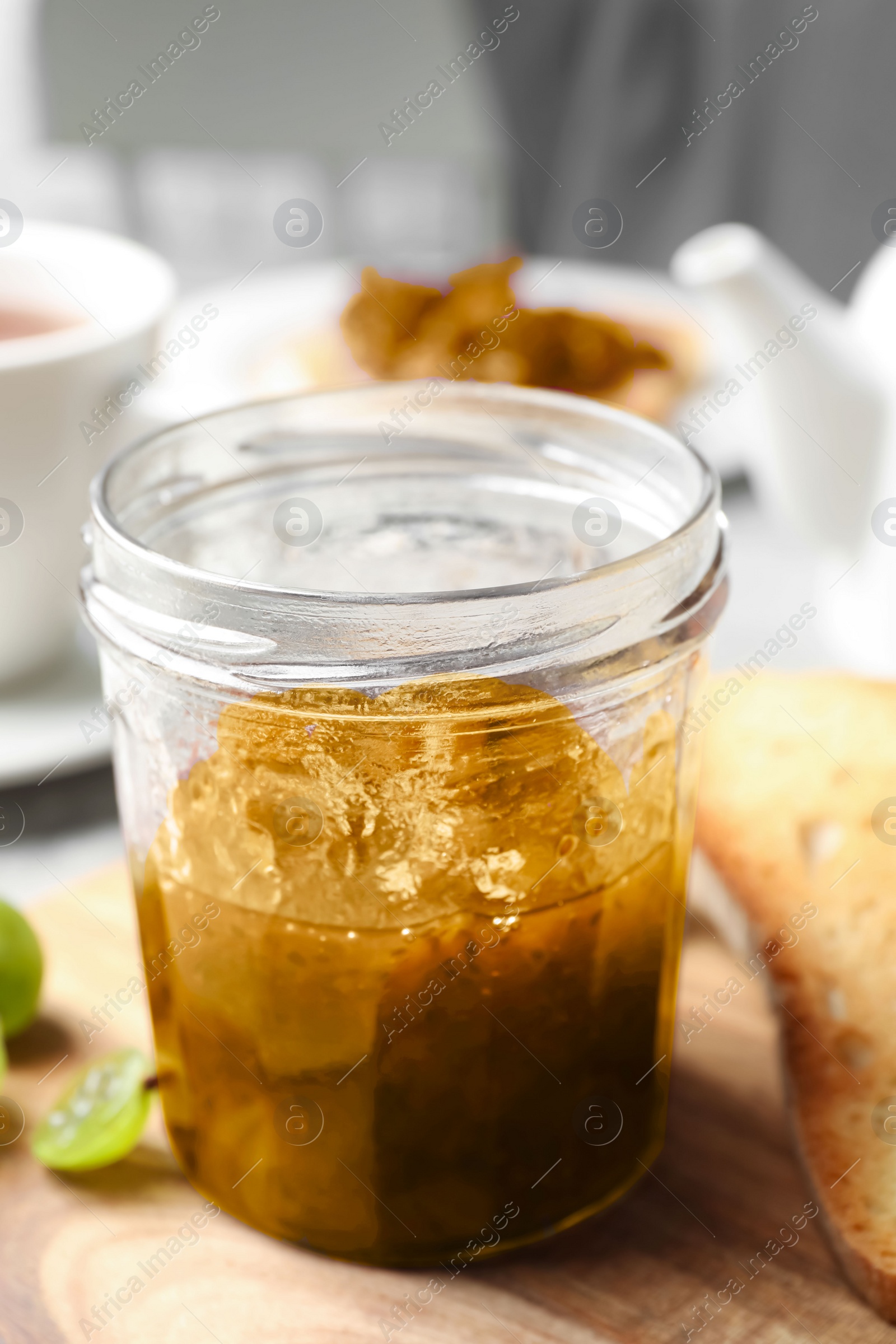 Photo of Jar of delicious gooseberry jam, toast and fresh berries on wooden board, closeup