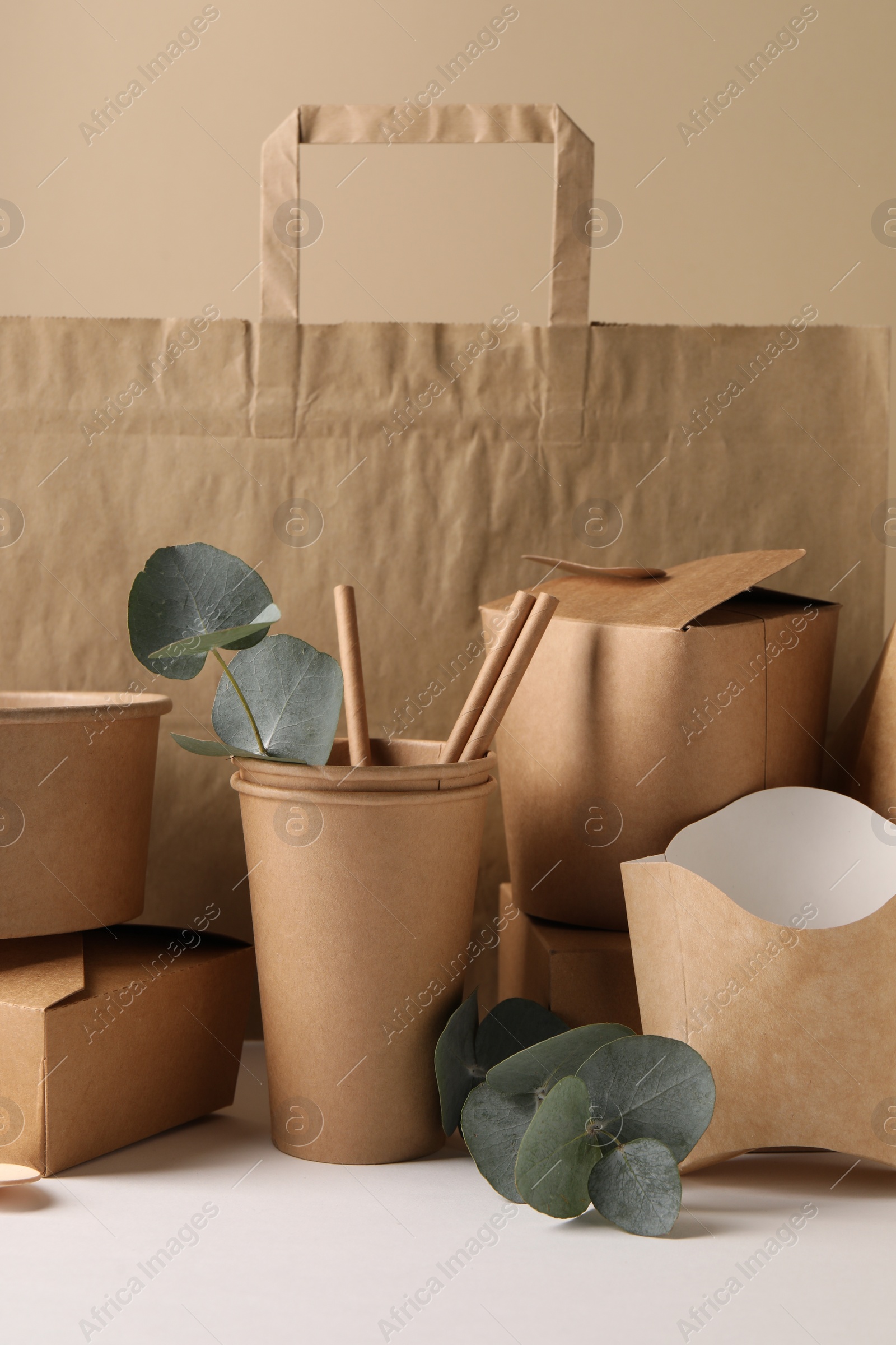 Photo of Eco friendly food packaging. Paper containers, tableware, bag and eucalyptus branches on white table against beige background