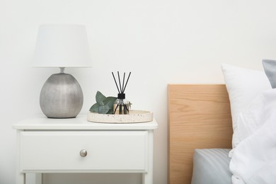 Photo of Reed diffuser with lamp and eucalyptus on nightstand in bedroom