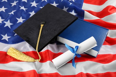 Photo of Black graduation hat, diploma and book on American flag