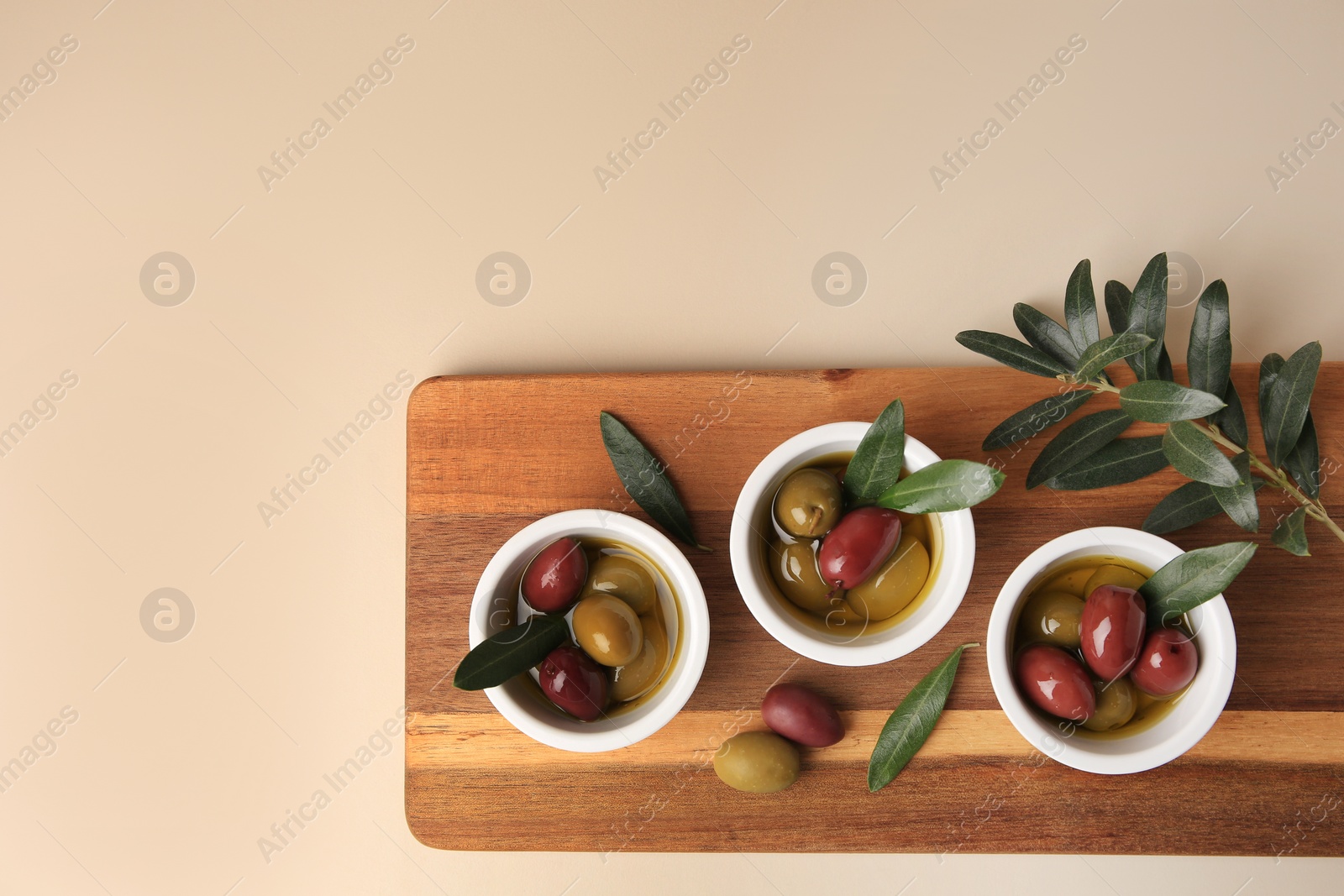Photo of Bowls with different ripe olives and leaves on beige background, flat lay. Space for text