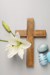 Wooden cross, painted Easter eggs and lily flowers on grey background, flat lay