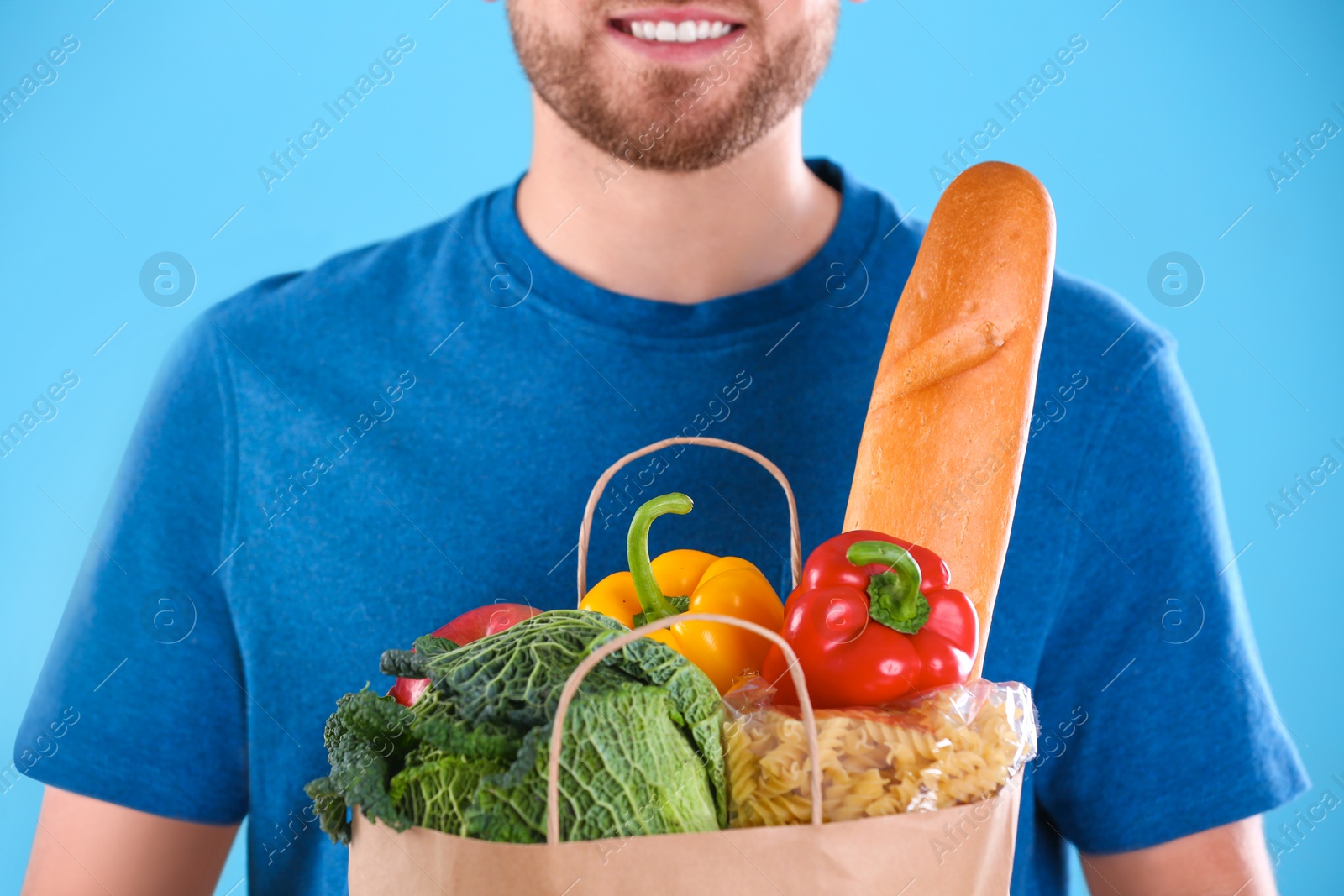 Photo of Delivery man holding paper bag with food products on color background, closeup