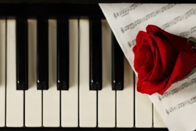 Photo of Beautiful red rose and musical notes on piano keys, top view. Space for text
