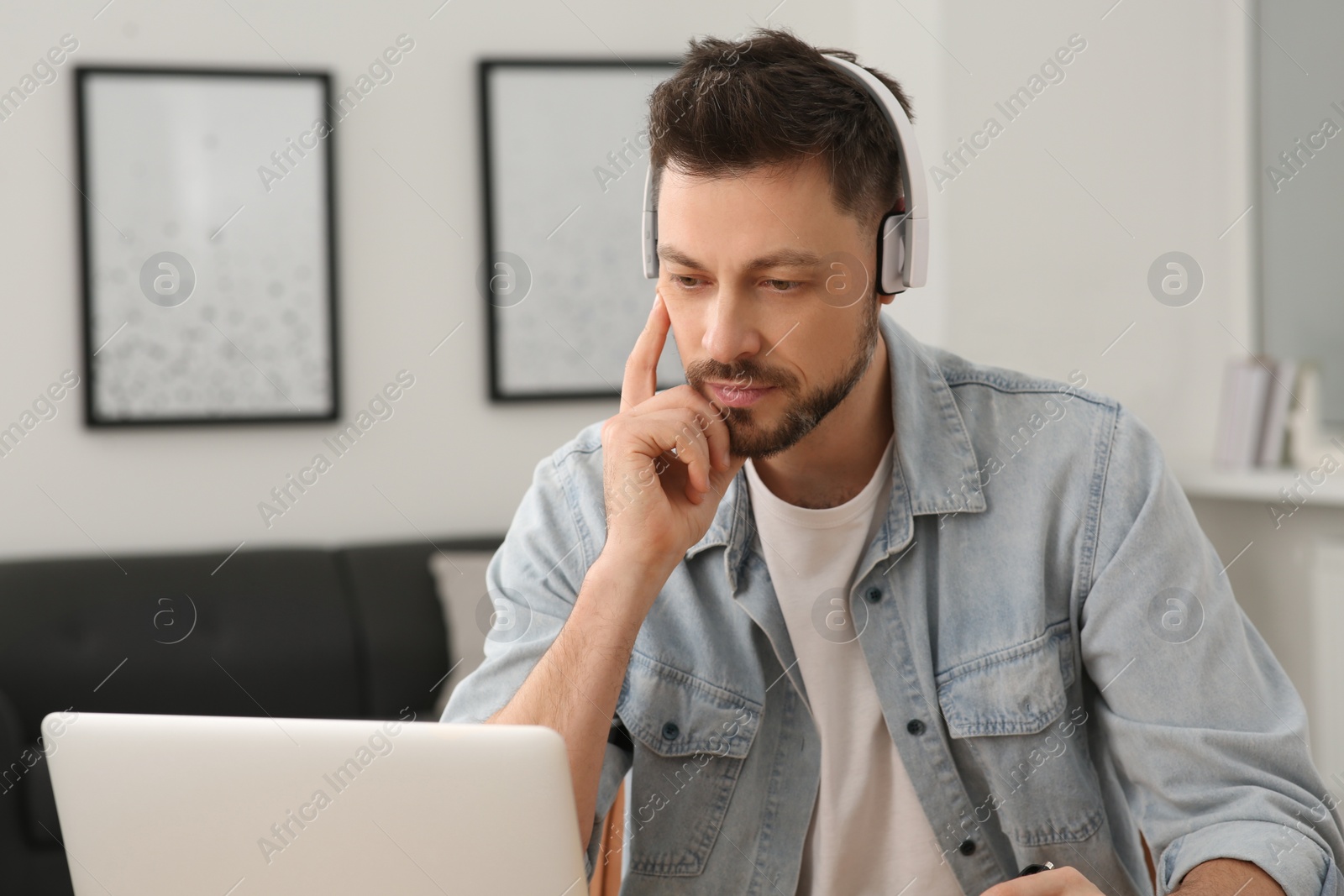 Photo of Man in headphones studying on laptop at home. Online translation course