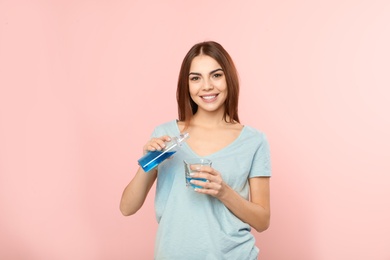 Photo of Beautiful woman pouring mouthwash from bottle into glass on color background. Teeth and oral care