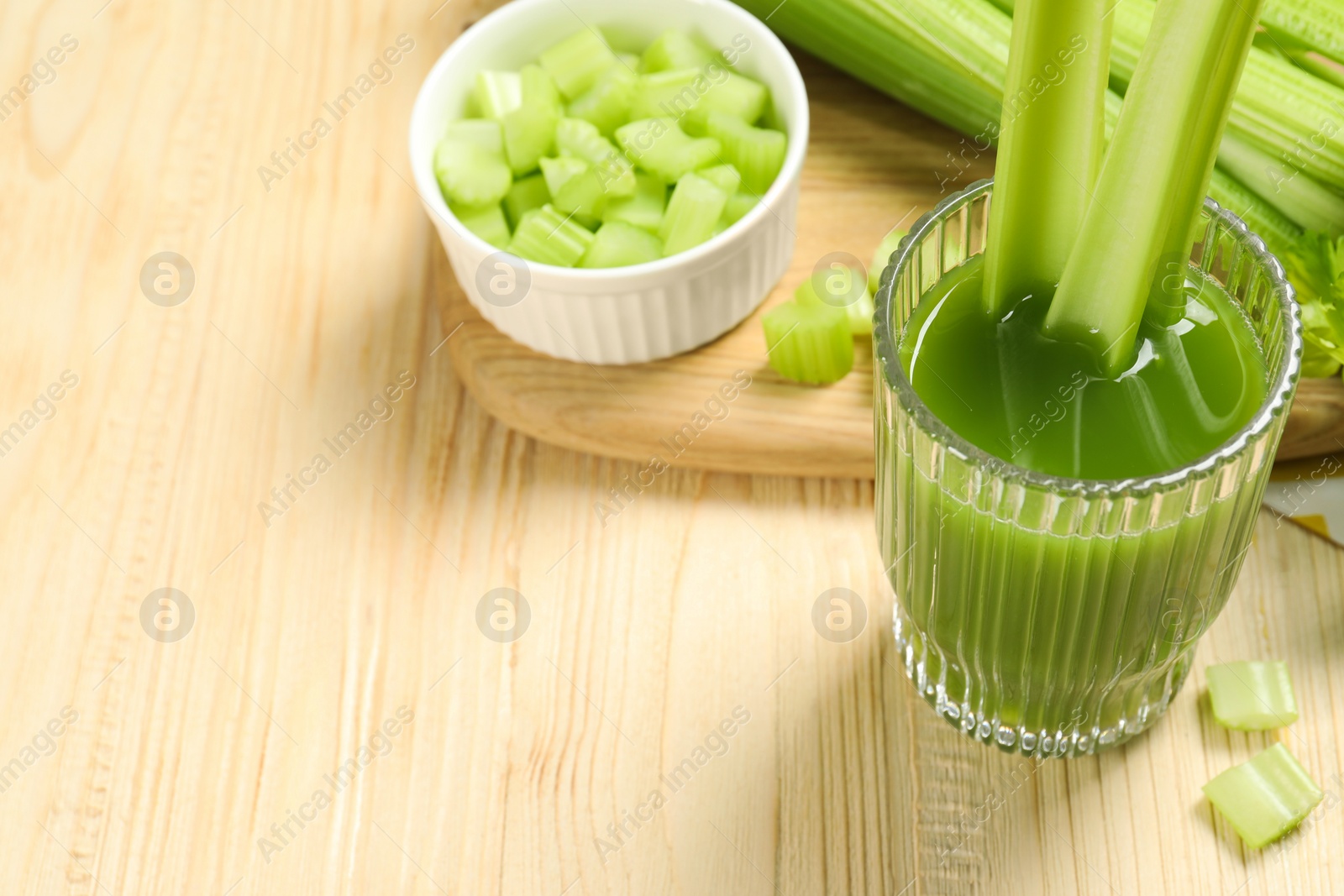 Photo of Glass of celery juice and fresh vegetables on wooden table. Space for text