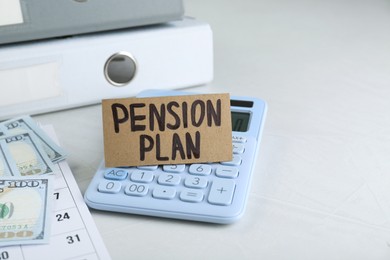 Photo of Card with phrase Pension Plan, calculator, dollar banknotes and calendar on white office table