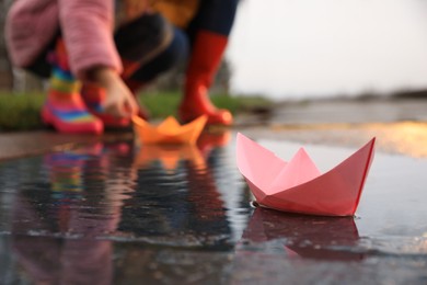Photo of Little girl and her mother playing near puddle outdoors, focus on paper boat