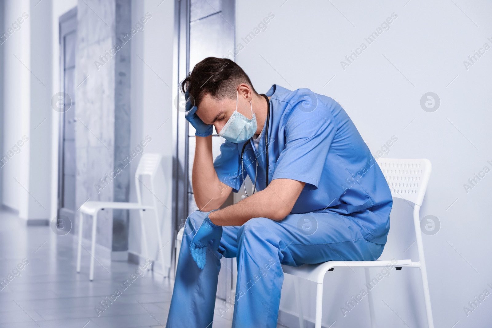 Photo of Exhausted doctor sitting on chair in hospital hallway