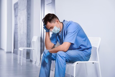 Exhausted doctor sitting on chair in hospital hallway