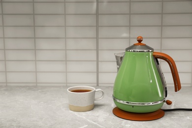 Photo of Modern electric kettle and cup of tea on grey marble kitchen counter. Space for text