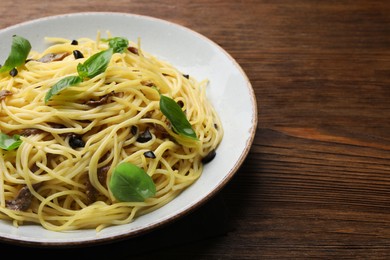 Photo of Delicious pasta with anchovies, olives and basil on wooden table, closeup. Space for text