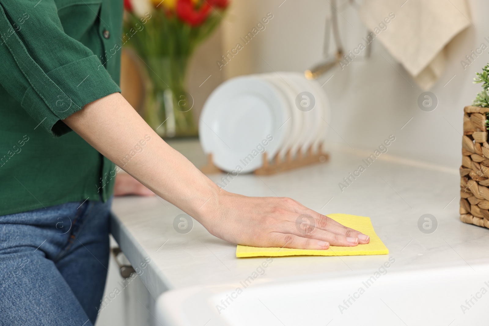 Photo of Woman cleaning table with sponge wipe in kitchen, closeup