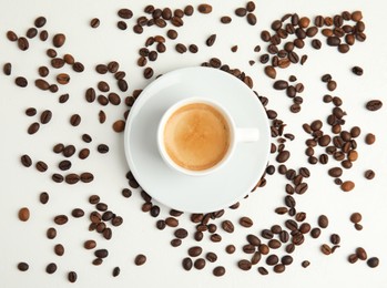 Photo of Cup of hot aromatic espresso and roasted beans on white table, flat lay