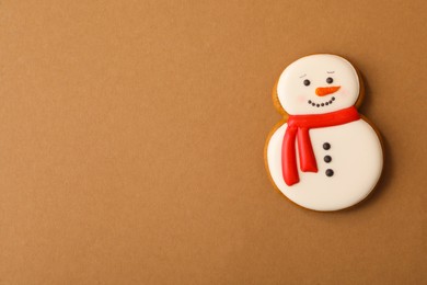 Photo of Christmas snowman shaped gingerbread cookie on brown background, top view. Space for text