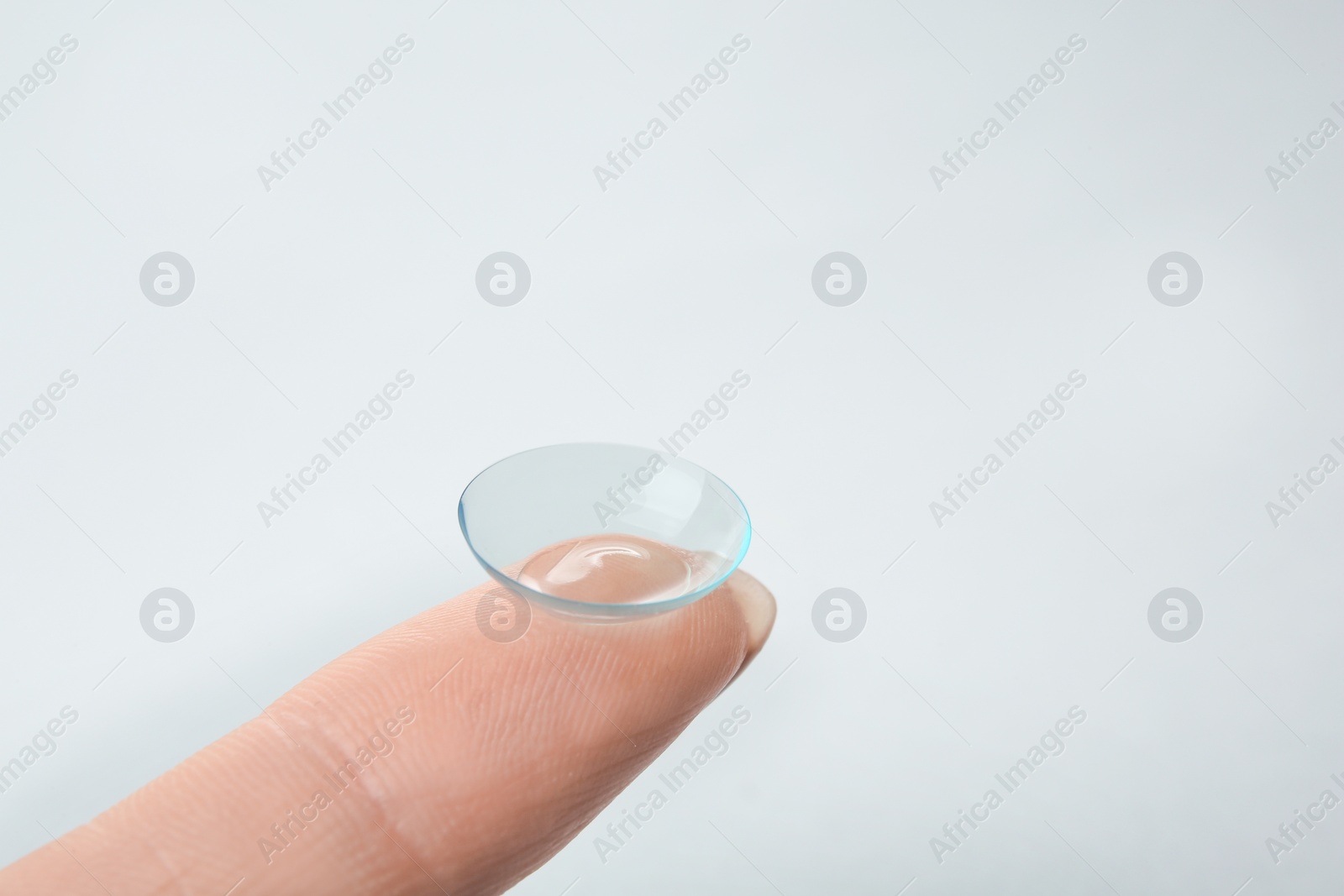 Photo of Woman with contact lens on light background, closeup