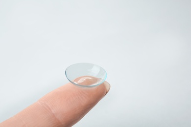 Photo of Woman with contact lens on light background, closeup