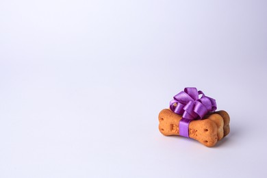 Photo of Bone shaped dog cookies with purple bow on white background. Space for text
