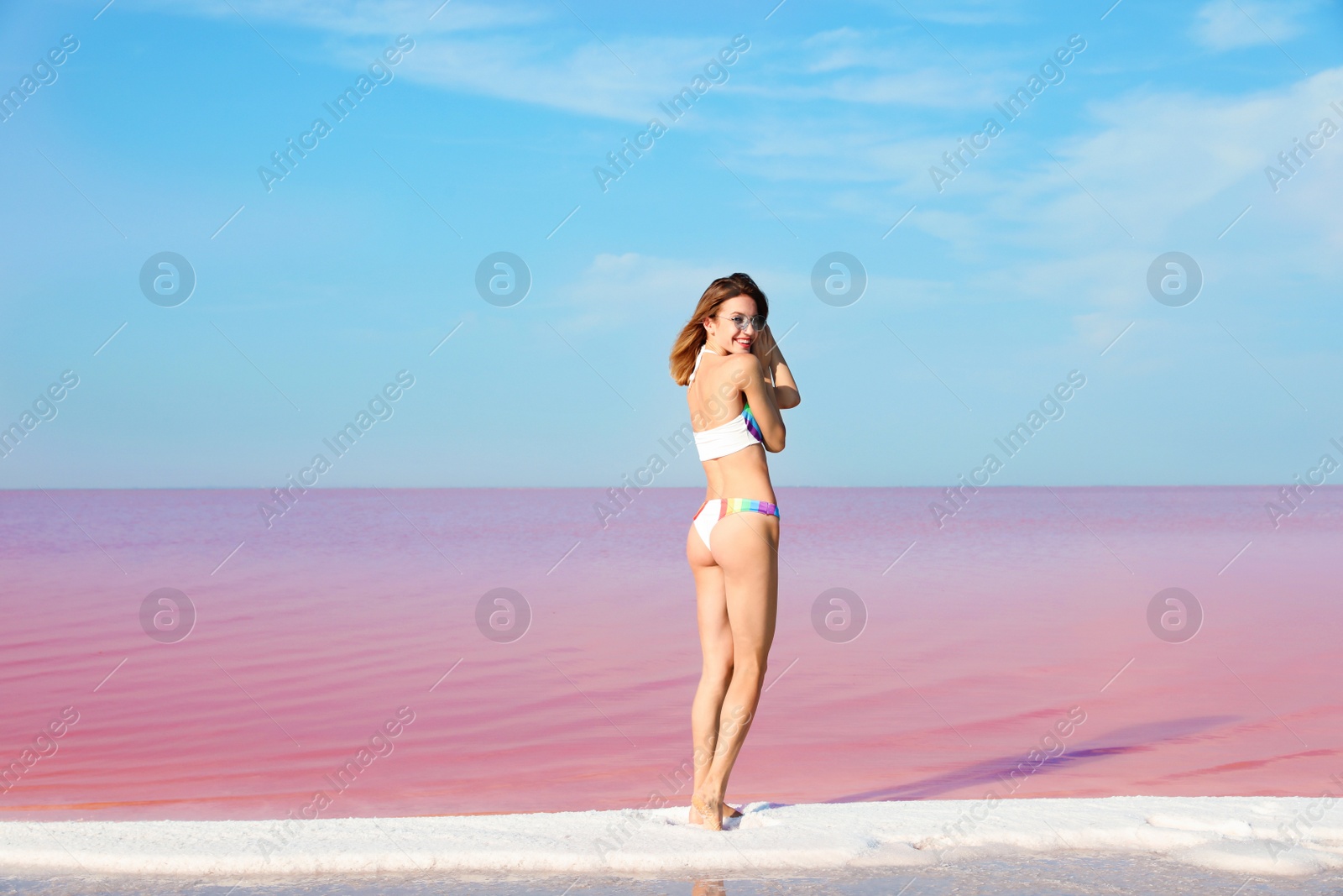 Photo of Beautiful woman in swimsuit standing near pink lake on sunny day