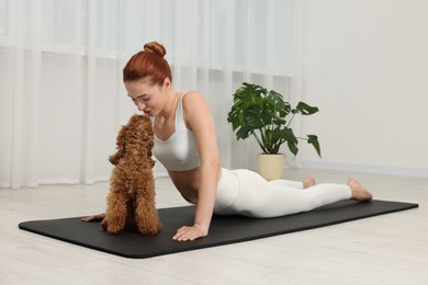 Young woman practicing yoga on mat with her cute dog indoors
