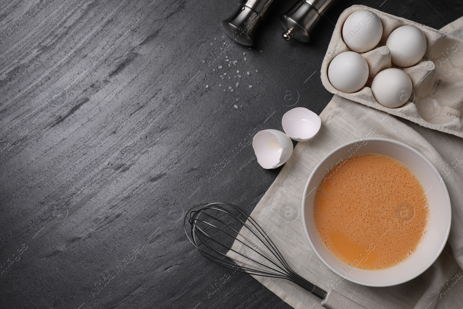 Photo of Metal whisk, beaten eggs and shells on dark grey background, flat lay. Space for text